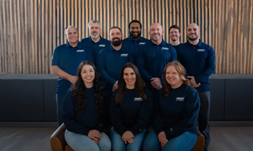 Prodigy Pest Solutions team group photo in navy uniforms in front of a wood slat wall