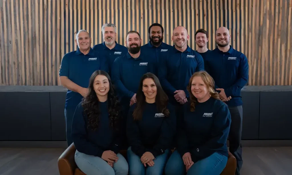 Prodigy Pest Solutions team group photo in navy uniforms in front of a wood slat wall
